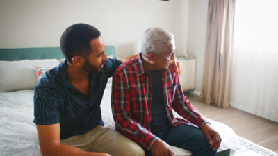 Adult Son Comforting Senior Father Suffering With Depression At Home